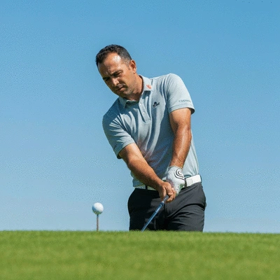 Professional golfer focusing intently on a golf ball before a swing, with a green course in the background. No text, no words, no typography, no labels, clean image