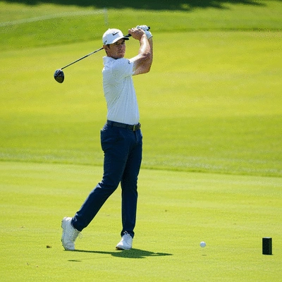 Professional golfer mid-swing on a pristine green course, showing focus and technique