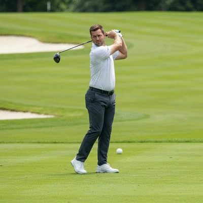 Professional golfer maintaining perfect spine angle during a swing on a green golf course, bright sunny day